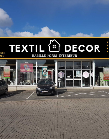 Vitrine d’un magasin Textil Décor avec un grand logo sur fond noir et des vitrines affichant des articles à l’intérieur.